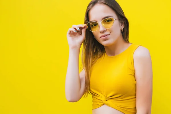 Портрет милої дівчини-підлітка в жовтому одязі та жовтих сонцезахисних окулярах на жовтому фоні . — стокове фото