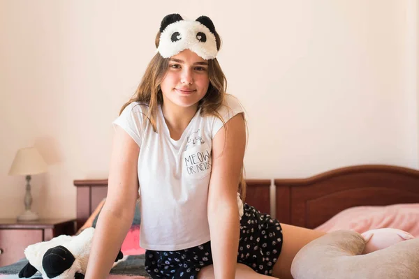 Милая девочка-подросток в своей постели в пижаме и панде в маске для сна . — стоковое фото