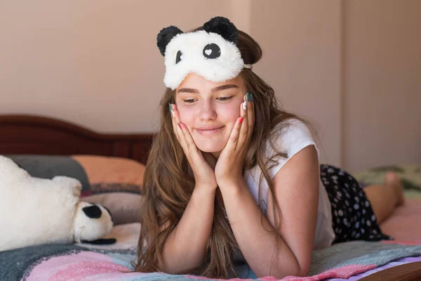 Cute teenage girl in her bed in pajamas and sleep mask panda. — ストック写真