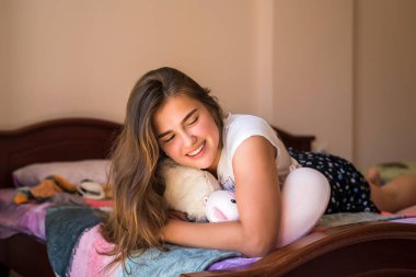 Portrait pretty cute teenage young girl on bed in modern apartment in the morning. Cute teenage girl lying and laughing in her bed in pajamas