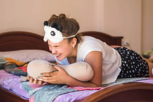 Linda adolescente acostada y riendo en su cama en pijama y la máscara del sueño panda . —  Fotos de Stock