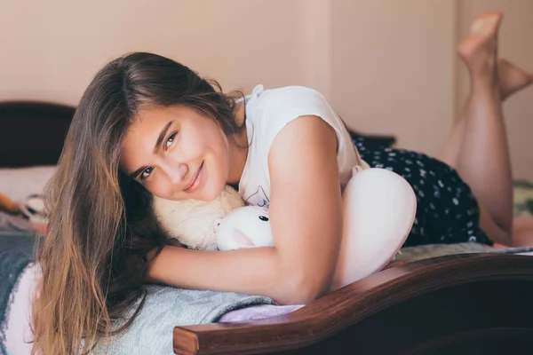 Портрет милої дівчини-підлітка на ліжку в сучасній квартирі вранці. Мила дівчина-підліток лежить і сміється в її ліжку в піжамі — стокове фото