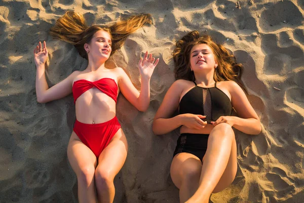 Concepto de moda vacaciones de verano. Dos adolescentes mintiendo y riendo en una playa tropical. Concepto vacaciones de verano . — Foto de Stock