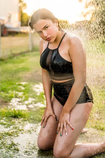 Bella giovane donna che si fa una doccia rilassante nella giornata di sole, all'aperto. Ritratto di chiusura. Giornata di sole. Vacanze tropicali fuga. L'acqua scorre attraverso il corpo della ragazza.Spruzzi d'acqua . — Foto Stock