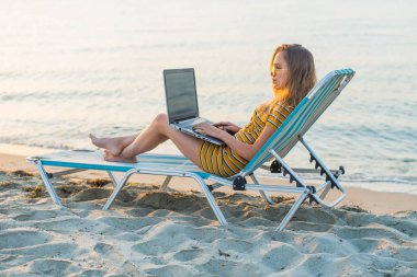 Kumsalda dizüstü bilgisayar kullanan genç bir kadın. Serbest çalışma kavramı