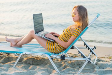 Kumsalda dizüstü bilgisayar kullanan genç bir kadın. Serbest çalışma kavramı