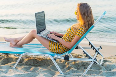 Kumsalda dizüstü bilgisayar kullanan genç bir kadın. Serbest çalışma kavramı