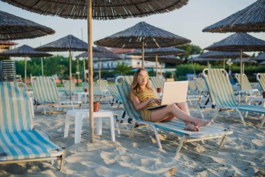 Kumsalda dizüstü bilgisayar kullanan genç bir kadın. Serbest çalışma kavramı