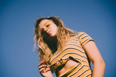 happy teenage attractive girl looks into the camera on the sunny beach over the blue sky wearing yellow sunglasses.