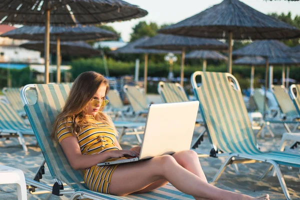 Mujer joven usando un ordenador portátil en una playa. Concepto de trabajo independiente — Foto de Stock