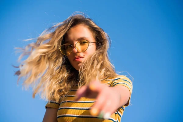 Adolescent heureux jolie fille regarde dans la caméra sur la plage ensoleillée sur le ciel bleu portant des lunettes de soleil jaunes . — Photo