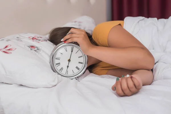 Mano debajo de la manta extendiéndose hacia fuera para el reloj despertador, Foto de pareja joven durmiendo en la cama mientras que la mujer estira la mano al reloj despertador para apagarlo. Enfoque en la mano con reloj —  Fotos de Stock