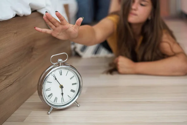 Sleepy young woman trying kill alarm clock . Early wake up, not getting enough sleep, getting work concept. Female stretching hand to ringing alarm willing turn it off