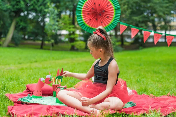 Fiesta de sandía, picnic para niños en el parque. Día de sandía. Linda niña pequeña con sombrero y con oso de juguete —  Fotos de Stock