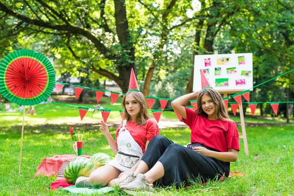 Zwei hübsche Teenie-Mädchen, die im Park Wassermelonen essen. Ausgezeichnetes sonniges Wetter. Sommerkonzept. Wassermelonenparty, Picknick, Tag — Stockfoto