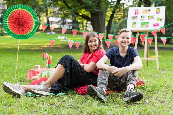 Nice teen girl and boy having fun watermelon party In the park. Excellent sunny weather. Summer concept. Watermelon party, picnic, day. — ストック写真