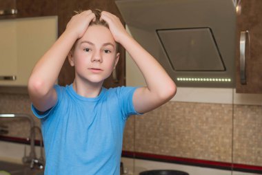 Handsome teenage boy cooking at the kitchen afraid and shocked with surprise expression, fear and excited face.