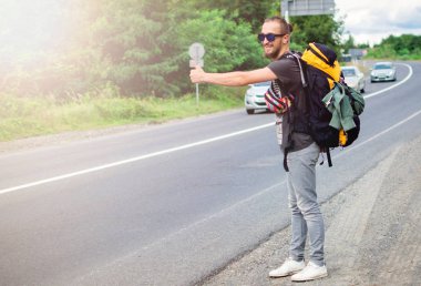 Modayı takip eden genç adam otobanın ortasında dikiliyor ve başka tarafa bakıyor. Sabah yolda yürüyen büyük sırt çantalı bir gezginin tam boy portresi. Maceradaki Duygusal Gezgin.
