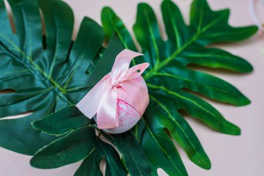 Pembe fiyonklu Paskalya yumurtası canavar yaprağının üzerinde yatıyor.