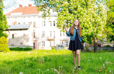 Bahar bahçesinde karahindiba üfleyen genç bahar moda kadını. İlkbahar. Bahar manzarasında günbatımında modaya uygun bir kız. Çiçeklerin polenine alerjisi var. Bahar alerjisi