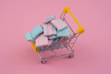 Yumuşak pembe arka planda lokum dolu bir alışveriş arabası.