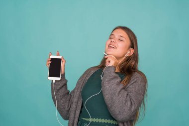 Moda oldukça tatlı, kaygısız genç kız kulaklıkla müzik dinliyor ve mavi arka planda akıllı telefonla şarkı söylüyor.