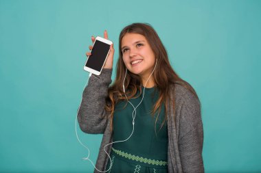 Modadan anlayan tatlı bir kız kulaklıkla müzik dinliyor, mavi arka planda pembe bir elbise giyiyor.