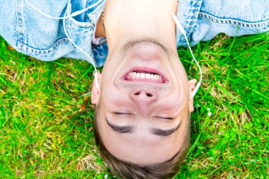 Kulaklıkla müzik dinleyen hoş bir genç adam. Çimlerin üzerinde yatarken.