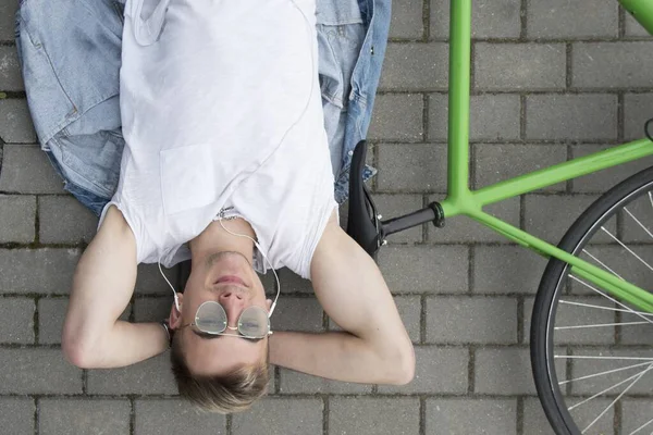 Bisikletli bir adam asfaltta yatıyor ve ata bindikten sonra rahatlıyor. Aktif yaşam tarzı. Bahar güneşli kavram.
