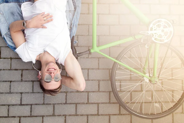 男人骑自行车躺在沥青路面上 骑马后放松 积极的生活方式 春日阳光普照 — 图库照片