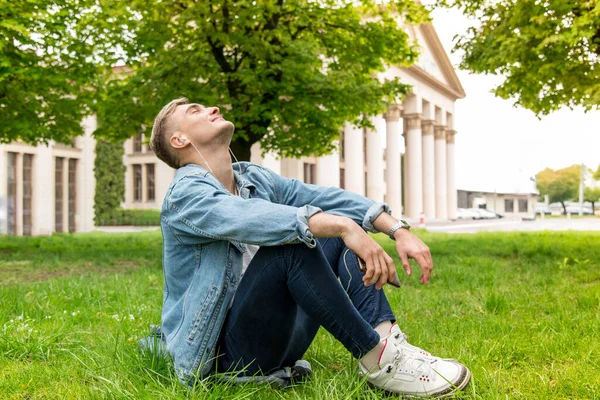 若い男がヘッドフォンで音楽を聴く 草の上に座っている男 — ストック写真