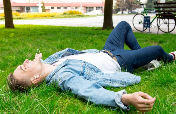ヘッドフォンで音楽を聴いている素敵な若い男 草の上に横たわる — ストック写真