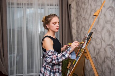 Yaratıcı mutlu ressam renkli bir tablo çizer. Gülümseyen pozitif kadın ressam atölyesinde resim yapıyor. Genç kız..