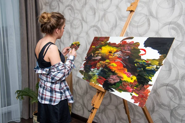 Smiling positive woman painter paints in her studio. Teenage girl.