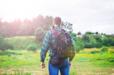 Yakışıklı hippi sakallı, ciddi yüzlü, kumaş gömlekli, askılı, açık havada, dağın tepesinde, bulutlu gökyüzüne karşı. Turizm konsepti. Sırt çantasıyla seyahat et. Muhteşem manzara..