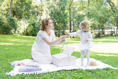 Parkta saman sepeti ve şapkayla piknik yapan güzel bir kız. Bahar güneşli konsept. Anneler Günün kutlu olsun. Sevgi dolu bir aile. Anne ve kızı..