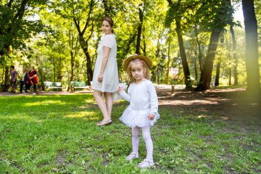 Hasır şapkalı küçük kızıyla yürüyen bir anne..