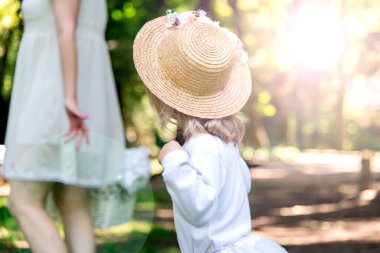 Hasır şapkalı küçük kızıyla yürüyen bir anne..