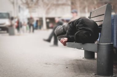 Fakir evsiz bir adam ya da şehirdeki şehir sokaklarında ahşap bankta uyuyan mülteci, sosyal belgesel konsepti, seçici odaklanma