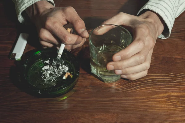 中毒の概念の灰皿でタバコを吸って飲むアルコールを抱きかかえたアルコールとガラスの手 — ストック写真