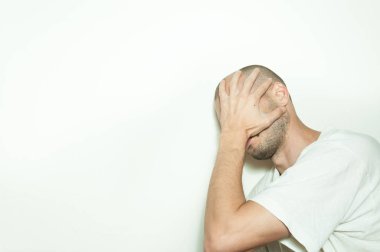 Genç adam acı yüzünü elleri ile akıl hastalığı anksiyete ve duygu mutsuz kapak ve beyaz duvara yaslanmış depresif