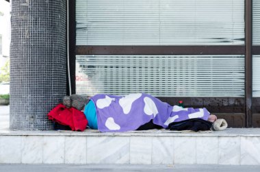 Tanınmayan evsiz yalınayak kadın uyku şehrin bina kaldırımda sokakta battaniye ile örtülü. 