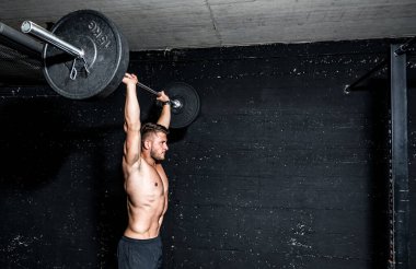 Genç, formda, kaslı, iri kaslı, halter kaldıran, ağırlık kaldıran spor salonunda egzersiz yapan kaslı bir adam.