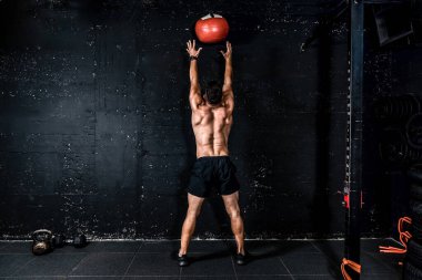 Genç, güçlü, terli, formda, kaslı, kaslı bir adam spor salonunda sıkı antrenman yapmak için duvarlara ilaç topu fırlatıyor.
