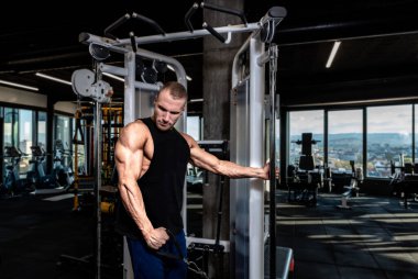 Genç, kaslı, terli, formda bir adam spor salonunda büyük kol kasları için kablo makinesinde antreman yapıyor.