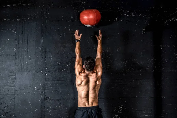 Genç, güçlü, terli, formda, kaslı, iri kaslı bir adam spor salonunda sıkı çalışmak için duvarlara ilaç topu fırlatıyor.