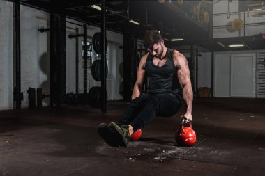 Genç, formda, terli, kaslı, tecrübeli bir adam spor salonunun zemininde ayaklarıyla ve bacaklarıyla amuda kalkıyor.