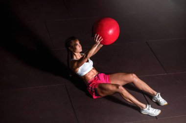 Genç, güçlü, terli, kaslı, iri kaslı bir kız karın kasları için ilaç topuyla mekik çekiyor ya da spor salonunda egzersiz yapıyor.