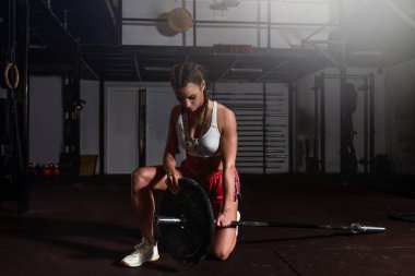 Güçlü kuvvetli kasları olan, halterci ya da ağırlık kaldırma antrenmanına hazırlanan genç, güçlü, kaslı bir kız. Spor salonunda halter ağırlıklarıyla egzersiz yapıyor. Gerçek insanlar spor yapıyor.