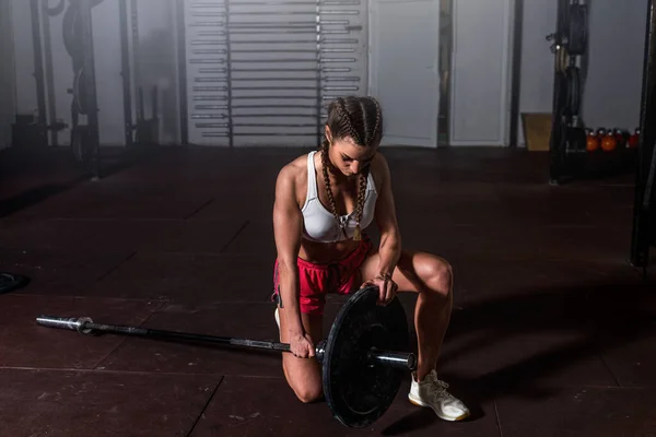 Young strong muscular fit girl with big muscles preparing for hard strength weightlifting or dead lift cross workout training with barbell weights in the gym real people exercising